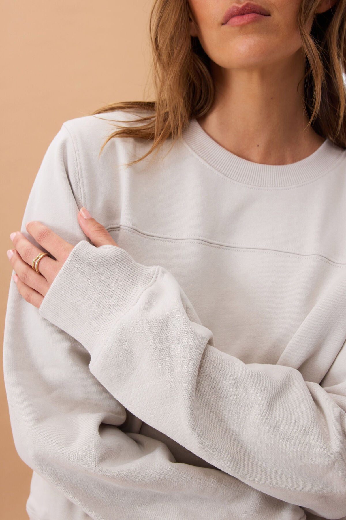 Person wearing an almond coloured sweatshirt against a beige background